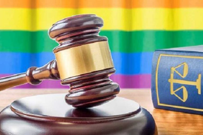 A gavel sits in front of a rainbow LGBTQ+ Pride flag.