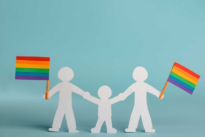 A paper doll cutout shows two adults with a child in the middle. They hold hands and carry rainbow Pride flags.