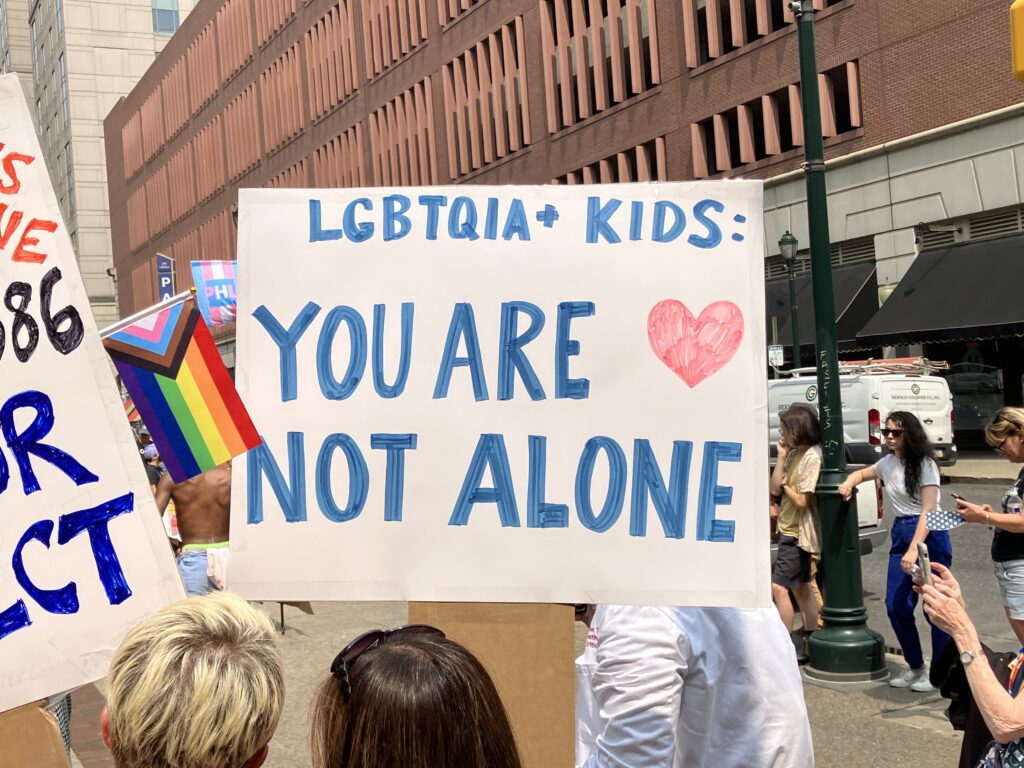 Moms for Liberty protest sign stating "LGBTQIA+ KIDS: YOU ARE NOT ALONE"