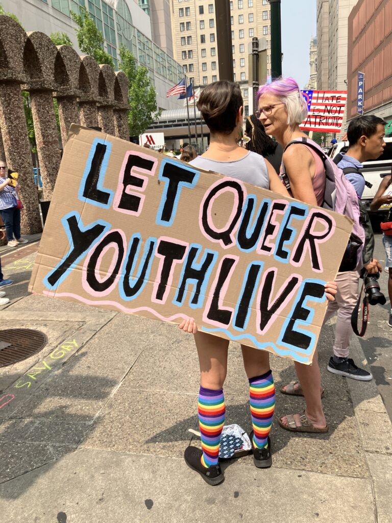 Moms for Liberty protest sign states "LET QUEER YOUTH LIVE"