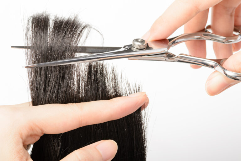 A hand is seen cutting the ends of hair against a white background.