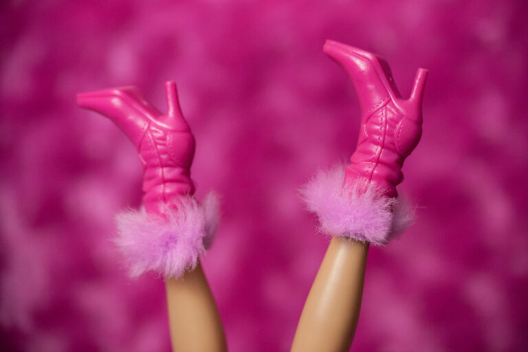 A Barbie Doll does a handstand to show off her pink high-heeled boots with furry cuffs