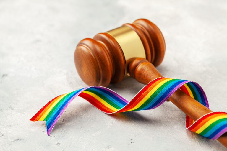 Judge gavel and rainbow ribbon of LGBT pride on gray background.