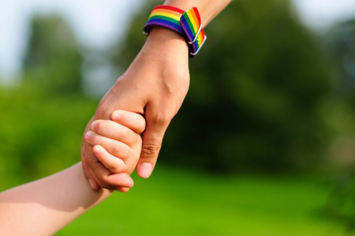 parent holds the hand of a small child. mother holding baby's hand. rainbow lgbt bracelet on parents hand