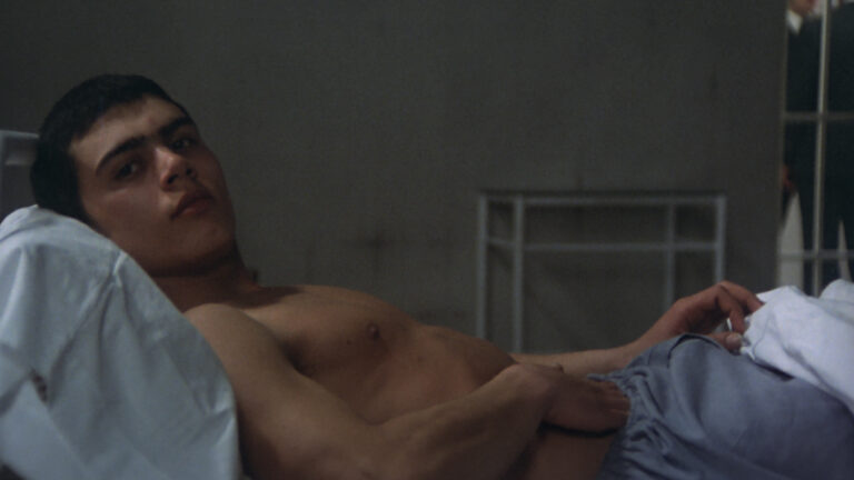 Ángel Pardo as Nes in ‘Confessions of a Congressman.’ Th actor lays on a bed, shirtless, as he sticks his hand down his pajama bottoms.