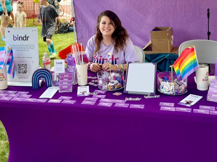 Mary Richardson sits at a table promoting Bindr at a Pride event.