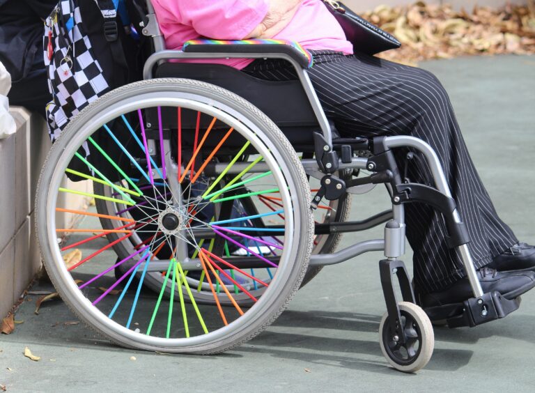 Mardi Gras Fair Day. A disabled woman in a wheel chair. The wheelchair is decorated in rainbow colours. WorldPride
