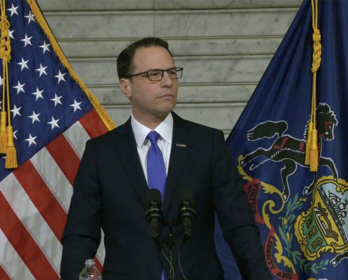 Pennsylvania Gov. Josh Shapiro speaks with the American flag and Pennsylvania flag behind him.