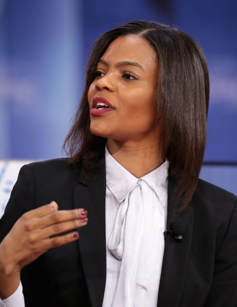 Candace Owens looks to her right. She is wearing a black blazer and white button down shirt.