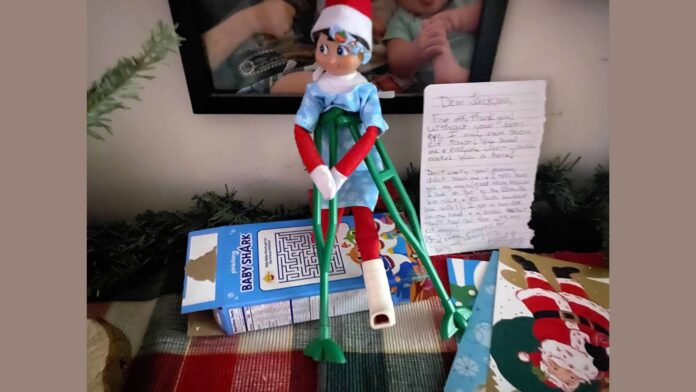 An Elf on the Shelf wears a hospital gown and sports crutches