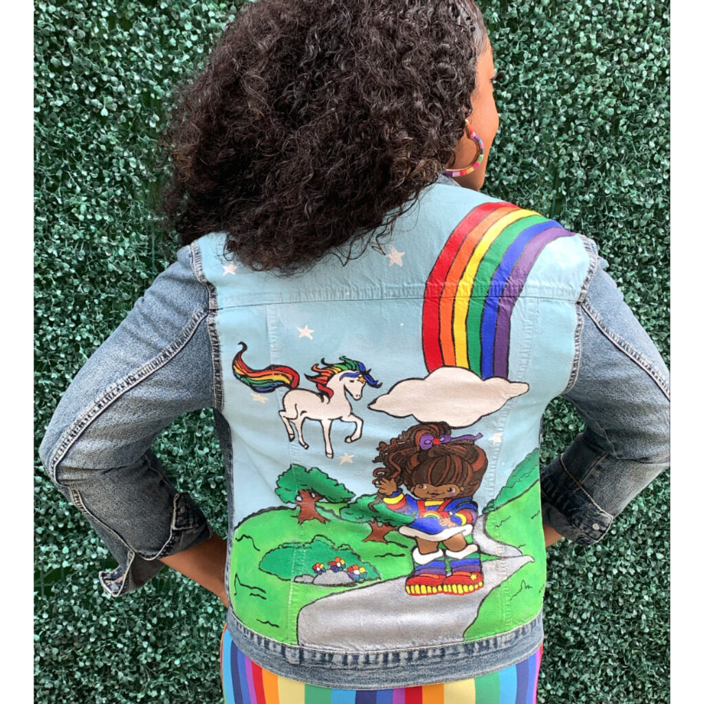 EsaDiva Maven wears a denim jacket featuring unicorns and rainbows.