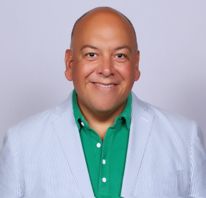 Jimmy Contreras wears a light blue blazer and kelly green polo shirt in a professional headshot. He smiles at the camera in front of a gray background.