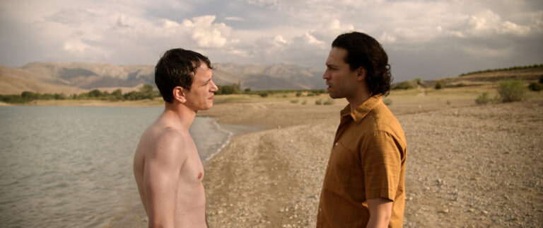 Two shirtless men on a beach in a scene from ‘Burning Days.’