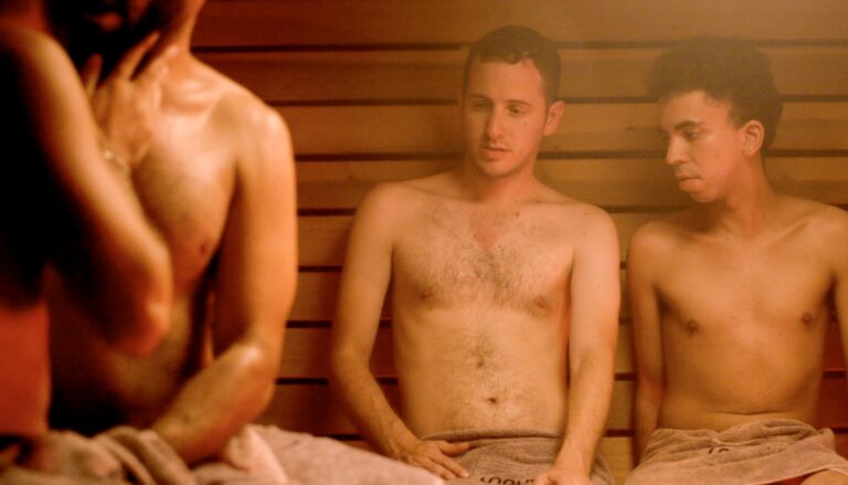 Nadav Portiansky in a scene from ‘Aloof.’ He is sitting in a gay sauna, or bath house, surrounded by men in towels.