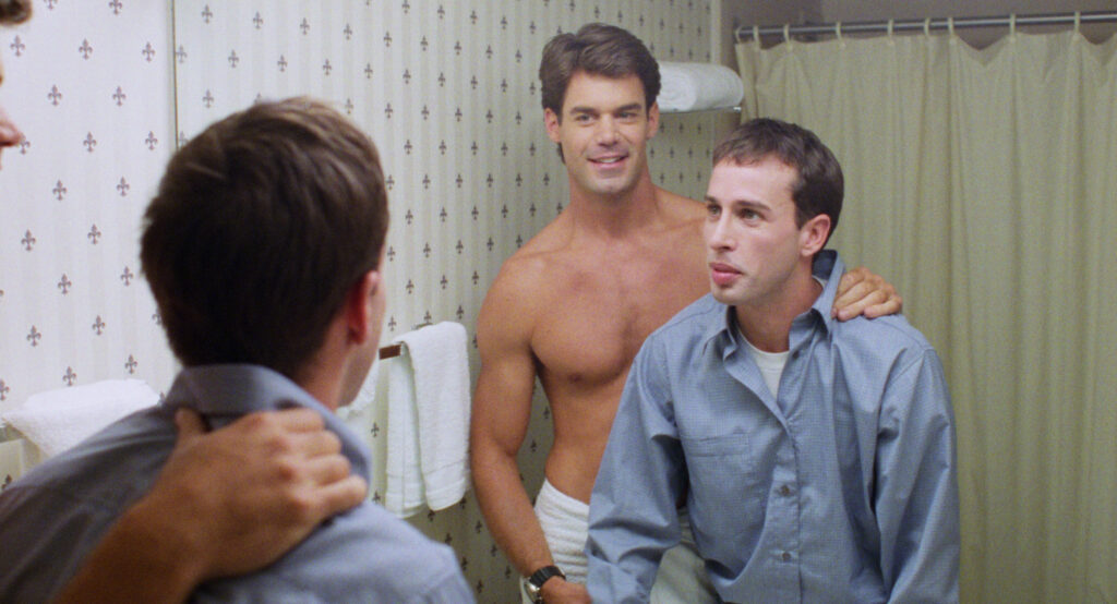 A scene from 'I Think I Do' where Tuc Watkins stands in a towel behind Alexis Arquette, who is wearing a light blue dress shirt.