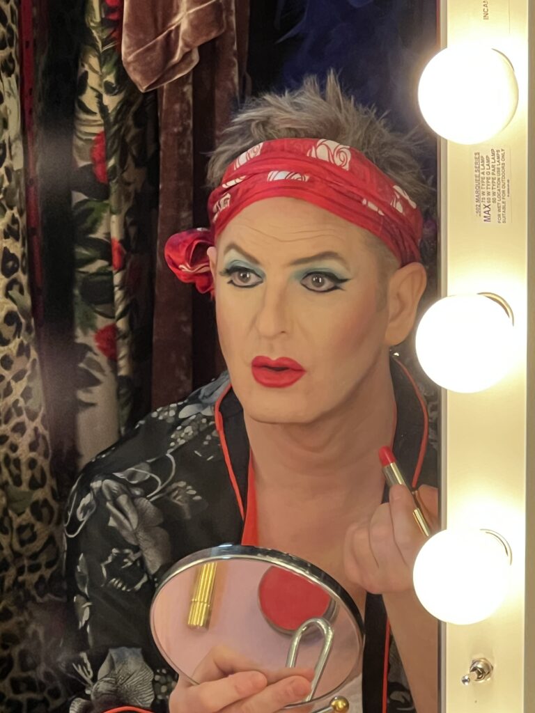 Jamison Stern as Arnold Beckoff in ‘Torch Song.’ Jamison is wearing lipstick, eyeshadow, eyeliner and a bandana as they look in the mirror.