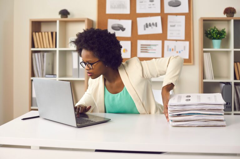 Convenient electronic bookkeeping vs stacks of papers. Secretary or financial accountant organizing digital documents on computer. Young woman sitting at office desk and doing paperwork on laptop