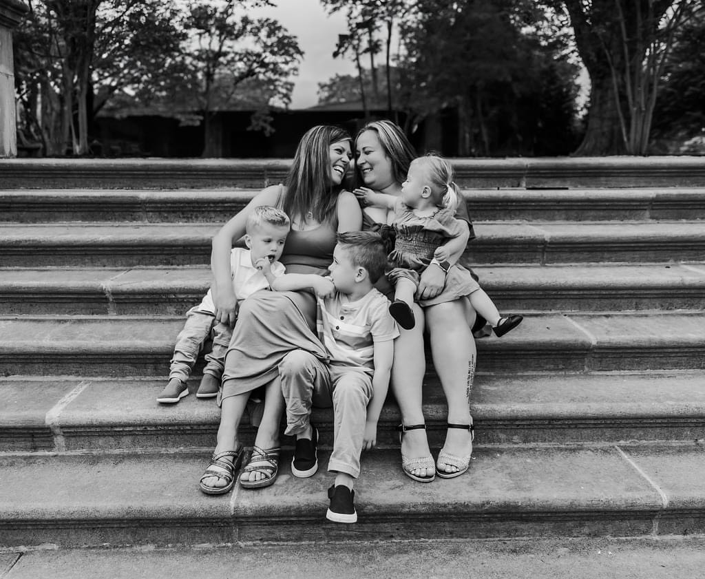 Black and white photo of two moms with three kids sitting on stair steps