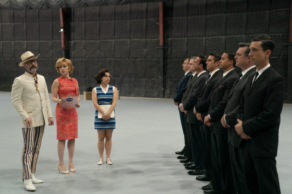 From left, Lance Vespertine (Jim Rash), Kelly Jones (Scarlett Johansson) and Ruby Martin (Anna Garcia) in ‘Fly Me to the Moon.’ The trio stand in front of men in suits.