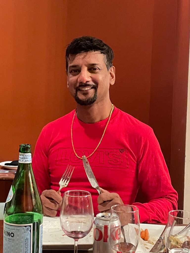 Anthony Logan sits at a table with a wine glass in front of him while holding a fork and knife.