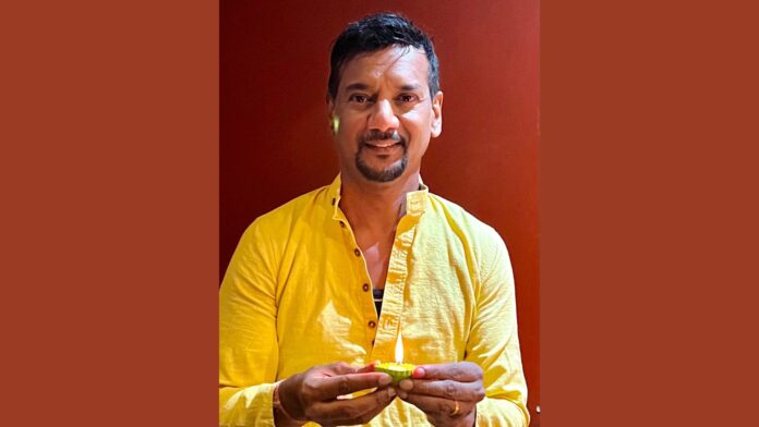 Anthony Logan wears a yellow button down shirt while holding a cupcake with a candle in it.