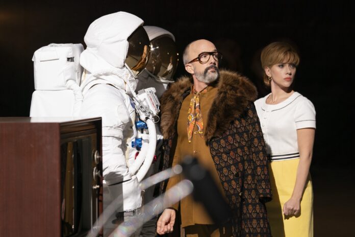 Jim Rash and Scarlett Johansson stand next to a space suit in a scene from Fly Me to the Moon.