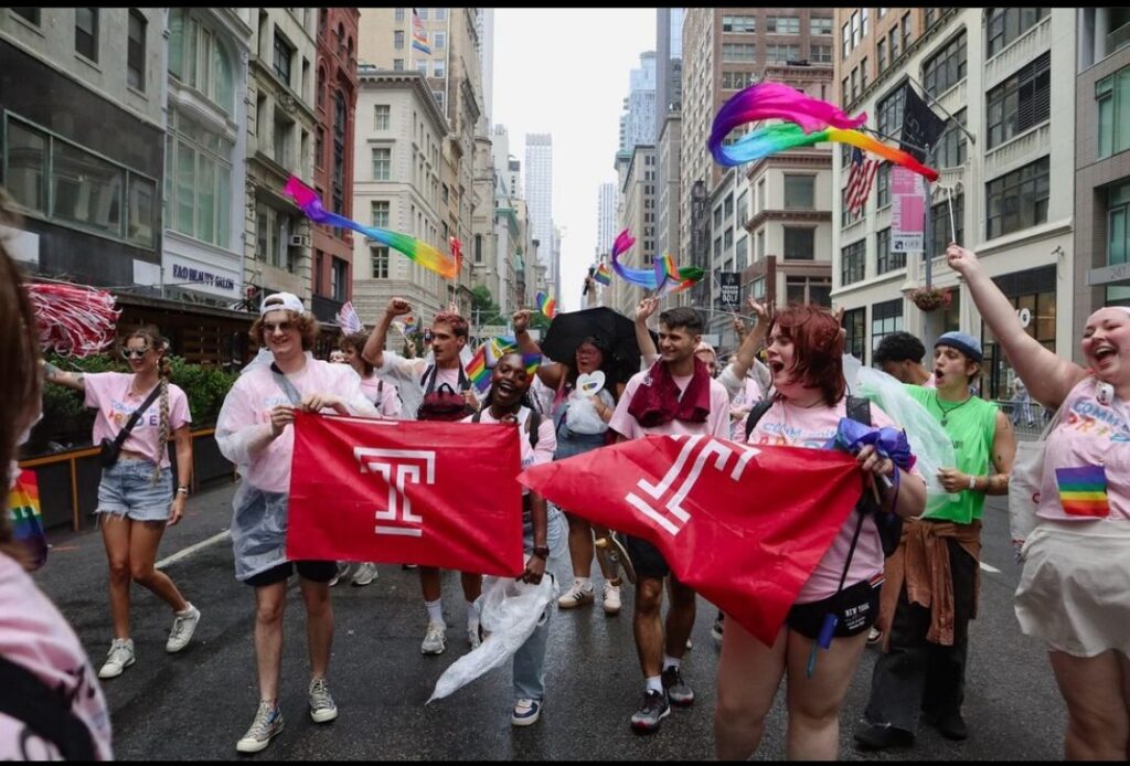 Temple students hold red banners with the University's logo and wave Pride flags as they walk through New York City streets.