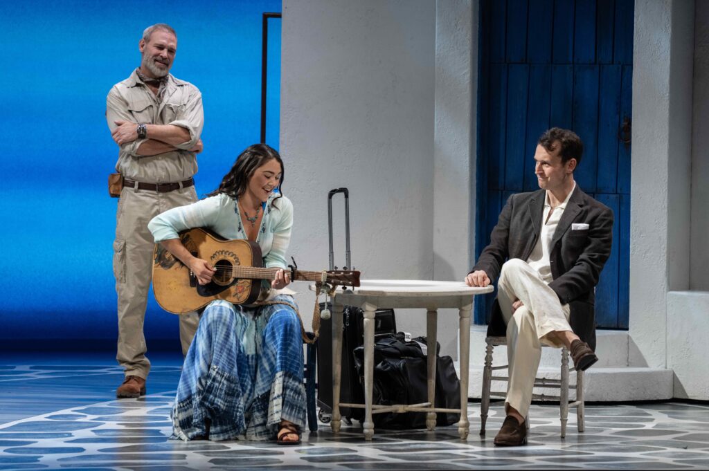 Jim Newman stands in the background looking lovingly at Alisa Melendez, who is playing a guitar as Rob Marnell also looks lovingly.