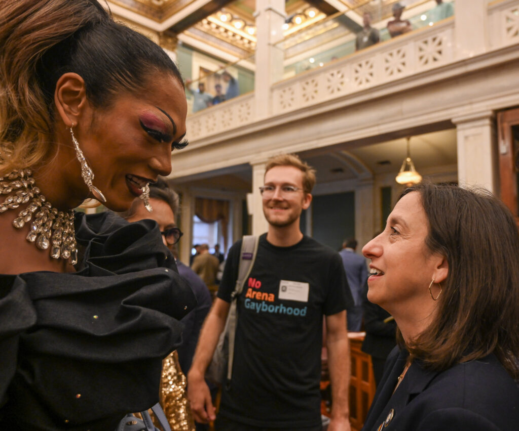 Shometha Monét leans forward to speak with council member Rue Landau inside City Hall. Another protester stands nearby, smiling as they talk.