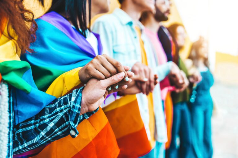 Group of lgbt people holding hands outside - Diverse happy friends hugging outdoors - Gay pride concept with crowd of guys and girls standing together on city street