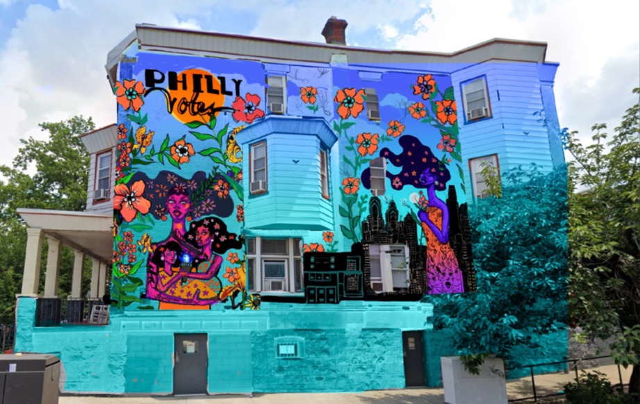 This image shows a vibrant mural painted on the side of a residential building, featuring the phrase "Philly Votes" in bold letters at the top. The mural is filled with large, colorful flowers and features several figures, including a woman with flowing hair surrounded by stars, holding a building in her hands. Another figure embraces two smaller figures, symbolizing unity, protection, or community. The backdrop includes the skyline of Philadelphia, blending urban elements with the natural floral designs, creating a powerful visual promoting civic engagement and local pride. The building itself is painted in various shades of blue, complementing the lively mural.