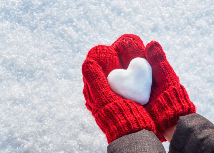 Female hands in knitted mittens with heart of snow in winter day