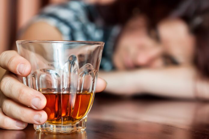 Drunk woman holding an alcoholic drink and sleeping with her head on the table (Focused on the drink, her face is out of focus)