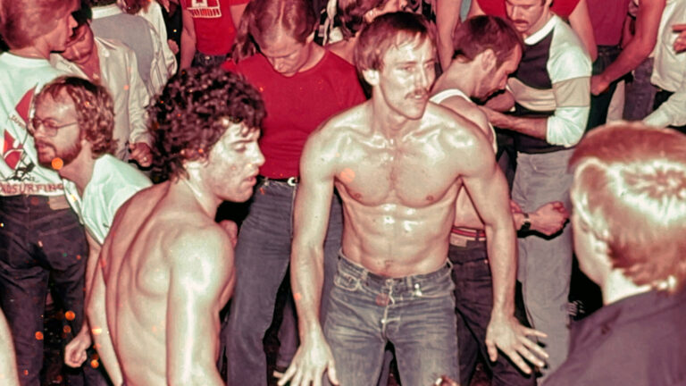 A lively scene from the documentary Studio One Forever featuring shirtless men dancing closely together in a crowded disco. The room is packed with partygoers, some dressed casually in t-shirts, while others are engaged in the vibrant energy of the moment. The image captures the camaraderie and intensity of Studio One's dance floor during its heyday.