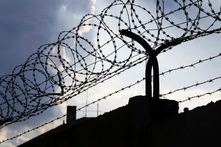 Dramatic clouds behind barbed wire fence on a prison wall