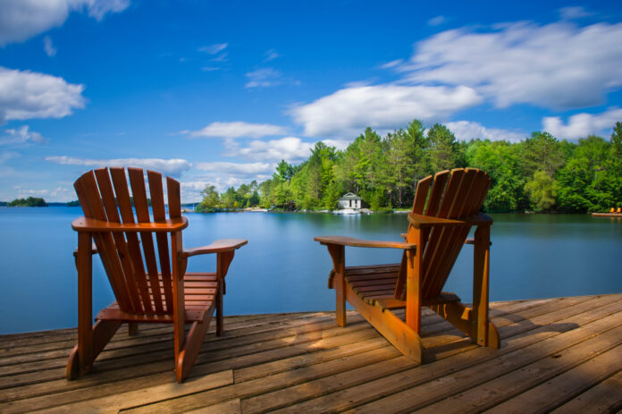 Two Muskoka chairs sitting on a wood dock facing a calm lake. Retirement concept