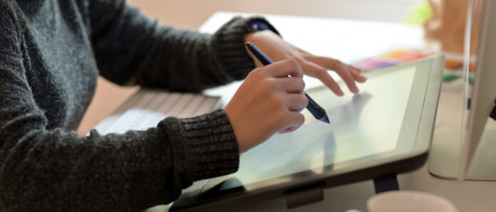 Side view of female graphic designer working on drawing tablet with stylus pen in office room