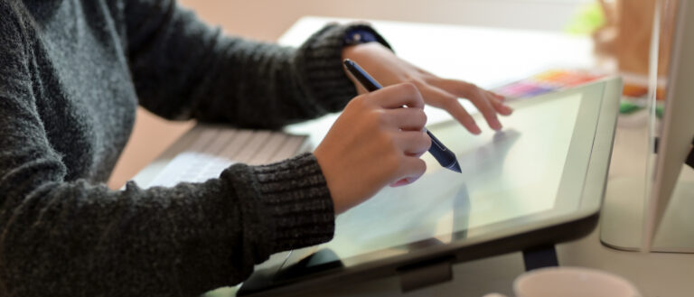 Side view of female graphic designer working on drawing tablet with stylus pen in office room